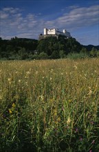 AUSTRIA, Salzburg, Hohensalzburg fortress situated on densely forested hillside above meadowland.