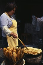 CHINA, Shanghai, "Woman using long pair of chopsticks to turn frying food in large, shallow dish in