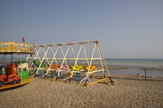 ENGLAND, West Sussex, Bognor Regis, Colourful children’s amusement rides on shingle beach