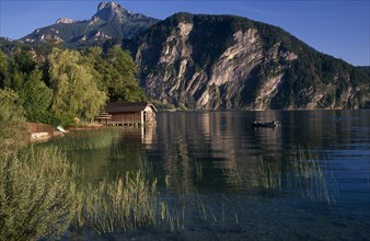AUSTRIA, Oberosterreich, Mondsee, "Small motor boat approaching boat house on shore of Monsee Lake