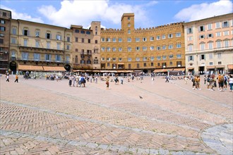 ITALY, Tuscany, Siena, People walking in the Piazza del Campo past the Palazzi and restaurants that