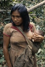 COLOMBIA, North West Amazon, Vaupes, Young Maku mother breast-feeding baby carried in sling across