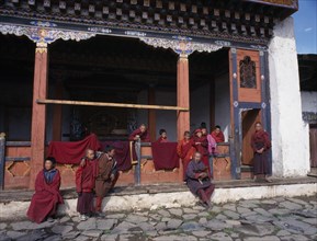 BHUTAN, Gantey Gompa, Group of young novice monks with older man holding cockerel gathered on step