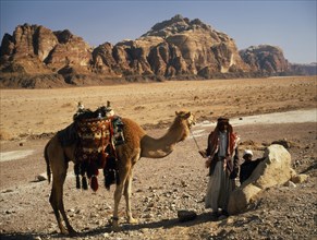 JORDAN, People, "Bedouin man and child standing beside camel carrying decorated, woven saddle and