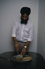 ENGLAND, Religion, Sikhism, Sikh man using short knife or kirpan to bless food.