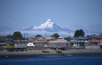 CHILE, Los Lagos, Architecture, Coastal village buildings near Chiloe from sea with snow capped