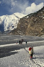 NEPAL, Annapurna Region, Khobang, Circuit Trek. Thakali villagers walking on the snow covered trail