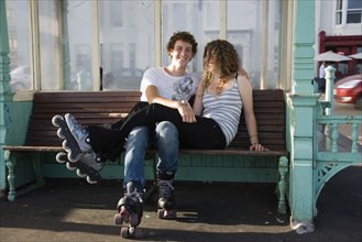 ENGLAND, East Sussex, Brighton, "Young couple sat on bench on the seafront promenade. One wearing