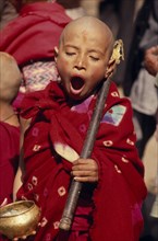 NEPAL, Kathmandu Valley, Bhaktapur, Young monk yawning during a ceremony and wearing red robes