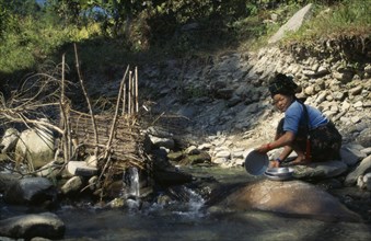 NEPAL, Manaslu Circuit Trek, Arughat, Woman washing pots beside a fish trap in a tributary river