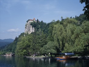 SLOVENIA, Lake Bled, Tourist boats on Lake Bled with castle partly seen amongst trees high above.