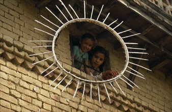 NEPAL, Kathmandu Valley, Children looking out of a window framed by the sun symbol of the Communist