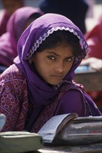 INDIA, Rajasthan, Jhunjhunu, A young girl student dressed in purple sitting at a desk with books at