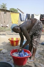 GAMBIA, Western Gambia, Tanji, Young woman bending to wash her family's clothes in a bowl before