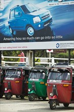 20091062 Tuk Tuks parked underneath advertising billboard Suzuki WagonR. Asia Asian Llankai Sri Lankan  Region - AsiaTransportMedia & CommunicationsDominant RedDominant Blue Jon Hicks 20091062 SRI...