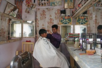 INDIA, Rajasthan, Jodhpur, Young Indian barber in his barbershop cutting a boys hair.