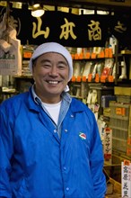 JAPAN, Honshu, Tokyo, Tsukiji fish market.  Three-quarter portrait of smiling Japanese man selling