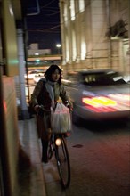 JAPAN, Honshu, Kyoto, Gion District.  Japanese woman riding her bicycle at night along a side road