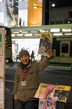 JAPAN, Honshu, Kyoto, "Japanese man selling the ‘Big Issue’ magazine, arm raised, holding copy with