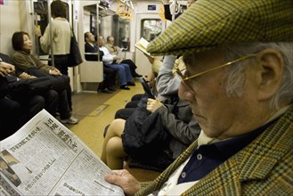 JAPAN, Honshu, Tokyo, Tokyo Metro.  Elderly Japanese man wearing tweed cap and jacket reading a
