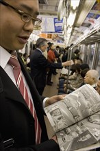 JAPAN, Honshu, Tokyo, Young Japanese man wearing a suit showing the Manga comic he is reading to