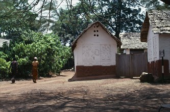 GHANA, Ashanti, Traditional thatched house with intricate patterns on walls. Man and woman walking