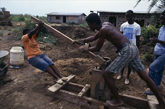 GHANA, Buduburam, Using hand operated machine worked by the action of a lever to make bricks.