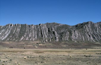 BOLIVIA, Altiplano, Vertically folded rock strata behind agricultural land with people and cattle