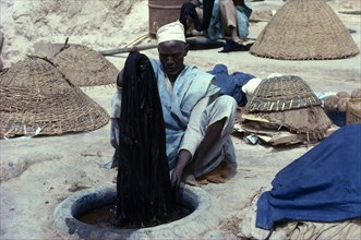 NIGERIA, Kano, Man dyeing cloth by hand in Indigo dye pits.