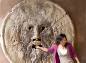 ITALY, Lazio, Rome, Woman with her hand in the jaws of The Bocca della Verita or Mouth of Truth