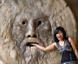 ITALY, Lazio, Rome, Woman with her hand in the jaws of The Bocca della Verita or Mouth of Truth