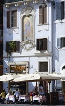 ITALY, Lazio, Rome, People seated outside a restaurant at tables in the shade of umbrellas below a