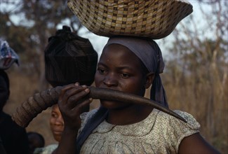 MALAWI, Tribal People, Yau Tribe, Yau woman blowing a water buck horn while carrying a load on her