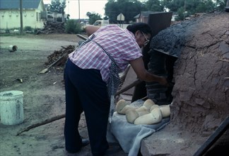 USA, New Mexico, Zuni, Zuni Native American Indian woman making bread in a Horno mud adobe outdoor