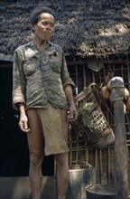 VIETNAM, Central Highlands, Dak Pek, Vietnam War. Montagnard standing next to thatched roof hut at