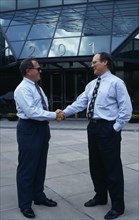 USA, Florida, Orlando, Two businessmen in conversation shaking hands outside modern glass fronted