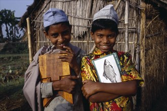 BANGLADESH, Shariatpur, "Three-quarter portrait of two, smiling young boys carrying books and