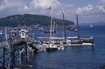 USA, Maine, Bar Harbour, "Wooden jetty with yacht moored at side, various boats on water and tree