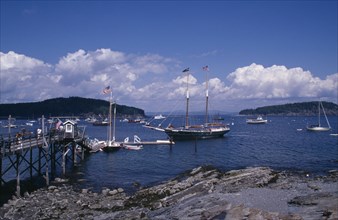 USA, Maine, Bar Harbour, "Wooden jetty with approaching yacht, various boats on water and tree