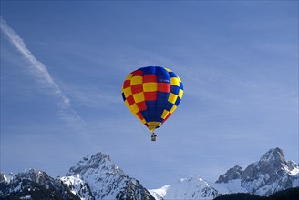 SWITZERLAND, Canton de Vaud, Chateau d'Oex, One Hot Air Balloon in flight above jagged snow covered