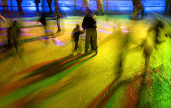 GERMANY, Bavaria, Munich, Ice Skaters in motion blur with multi coloured light on a winter ice rink