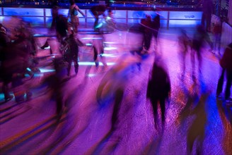 GERMANY, Bavaria, Munich, Ice Skaters in motion blur with multi coloured light on a winter ice rink