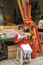 CHINA, Sichuan Province, Chongqing, Boy incense seller reading book outside the Arhat Temple in