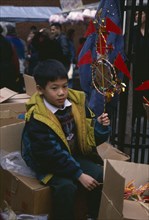 ENGLAND, London, Chinese New Year, Young boy sitting on boxes holding up decoration for New Year