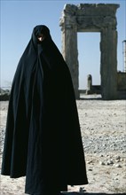IRAN, Fars Province , Persepolis, Full length standing portrait of a woman wearing a black Chador