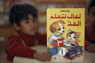 KUWAIT, Education, School boy reading a colourful book illustrated with a kitten and puppy