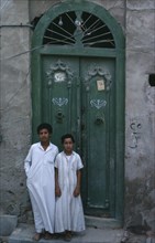 KUWAIT, People, Children, Two boys wearing long white robes standing outside a green doorway