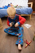 RELIGION, Festivals, Christmas, Young red headed boy in his pyjamas playing on the floor with his