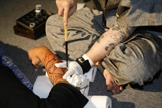 THAILAND, Phuket, Man having tattoo applied to arm.
