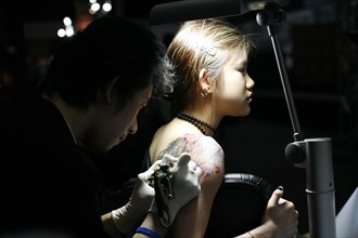 THAILAND, Phuket, Girl having tattoo applied to her shoulder.